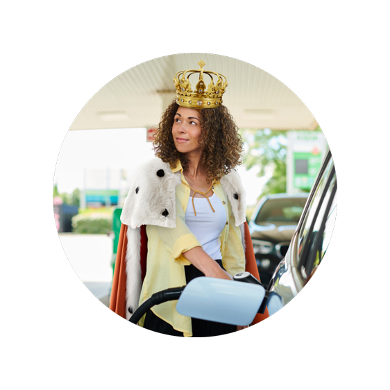 Woman wearing a crown and cape fills up her car with fuel