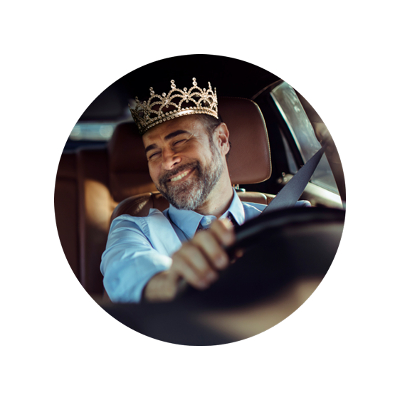 Male driver wears a crown and smiles within his car