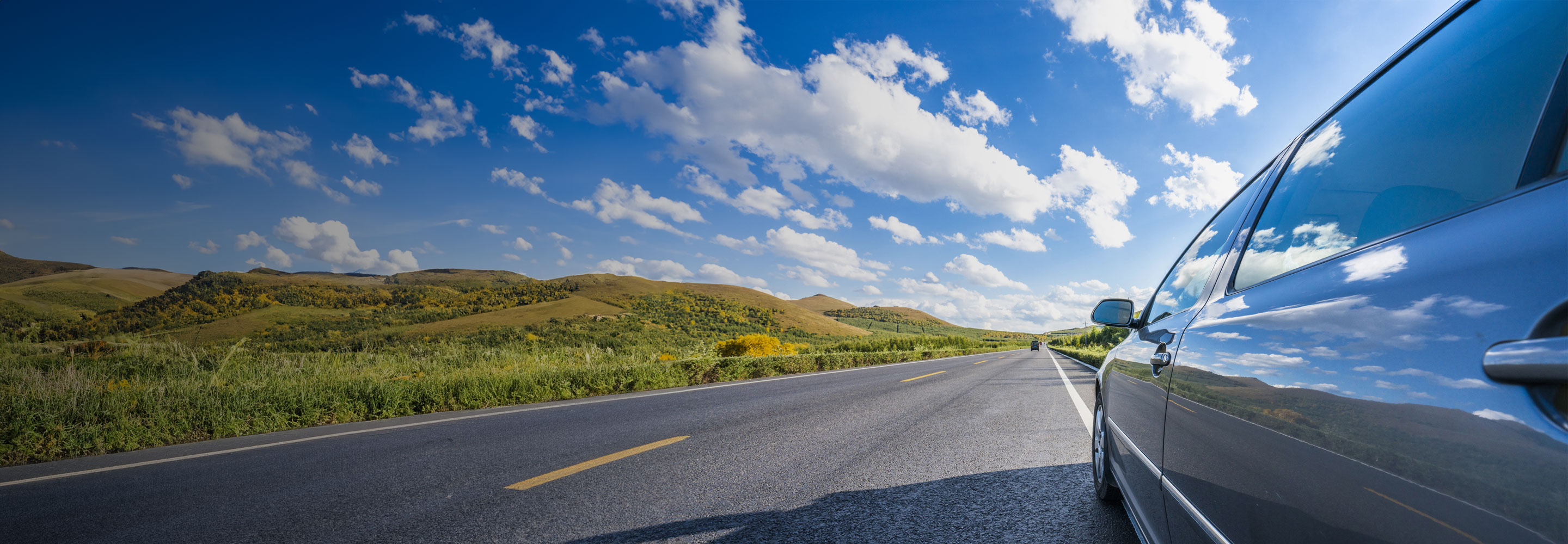Black car driving down a long road on a sunny day