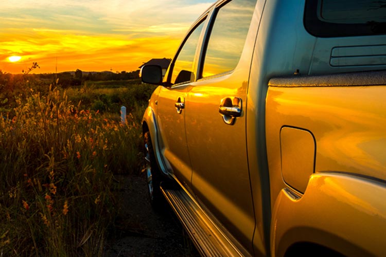 Pickup truck driving into the sunset on a grassy field