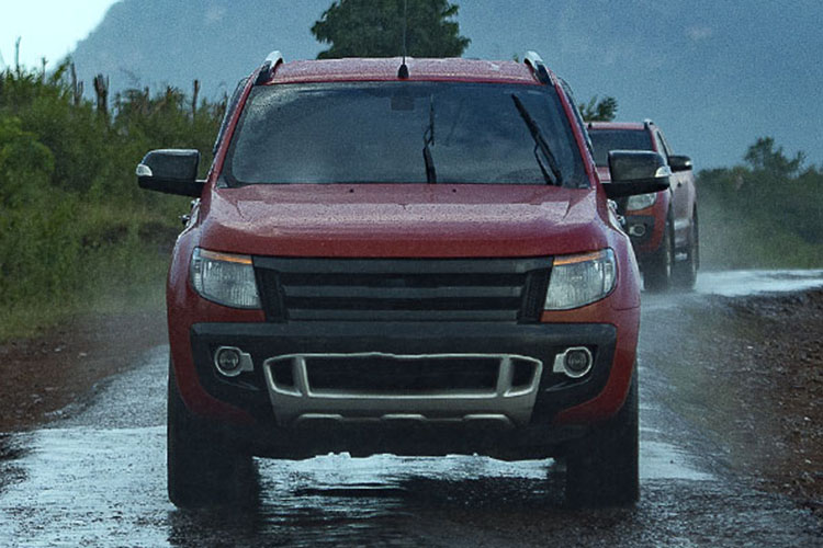 Red pick up truck driving down a tree lined highway in the rain