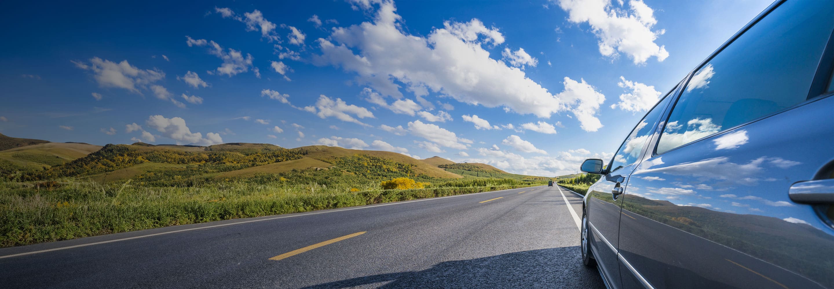 Black car driving down a long road on a sunny day