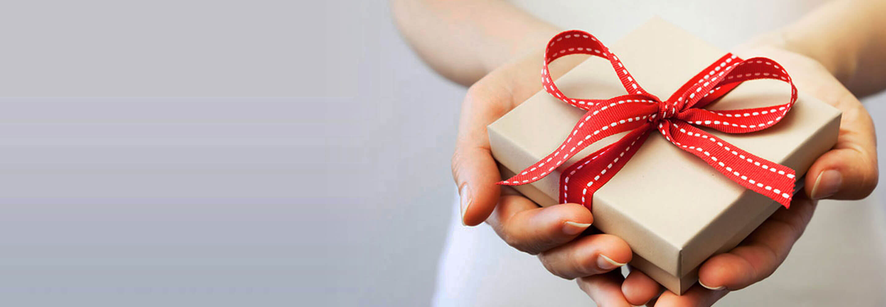 Two hands holding a gift box with a red ribbon